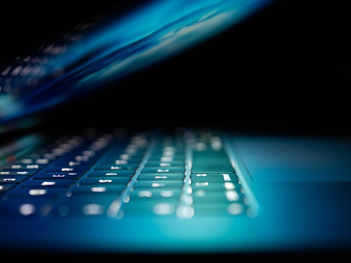 Close-up of a laptop keyboard glowing blue in a darkened room