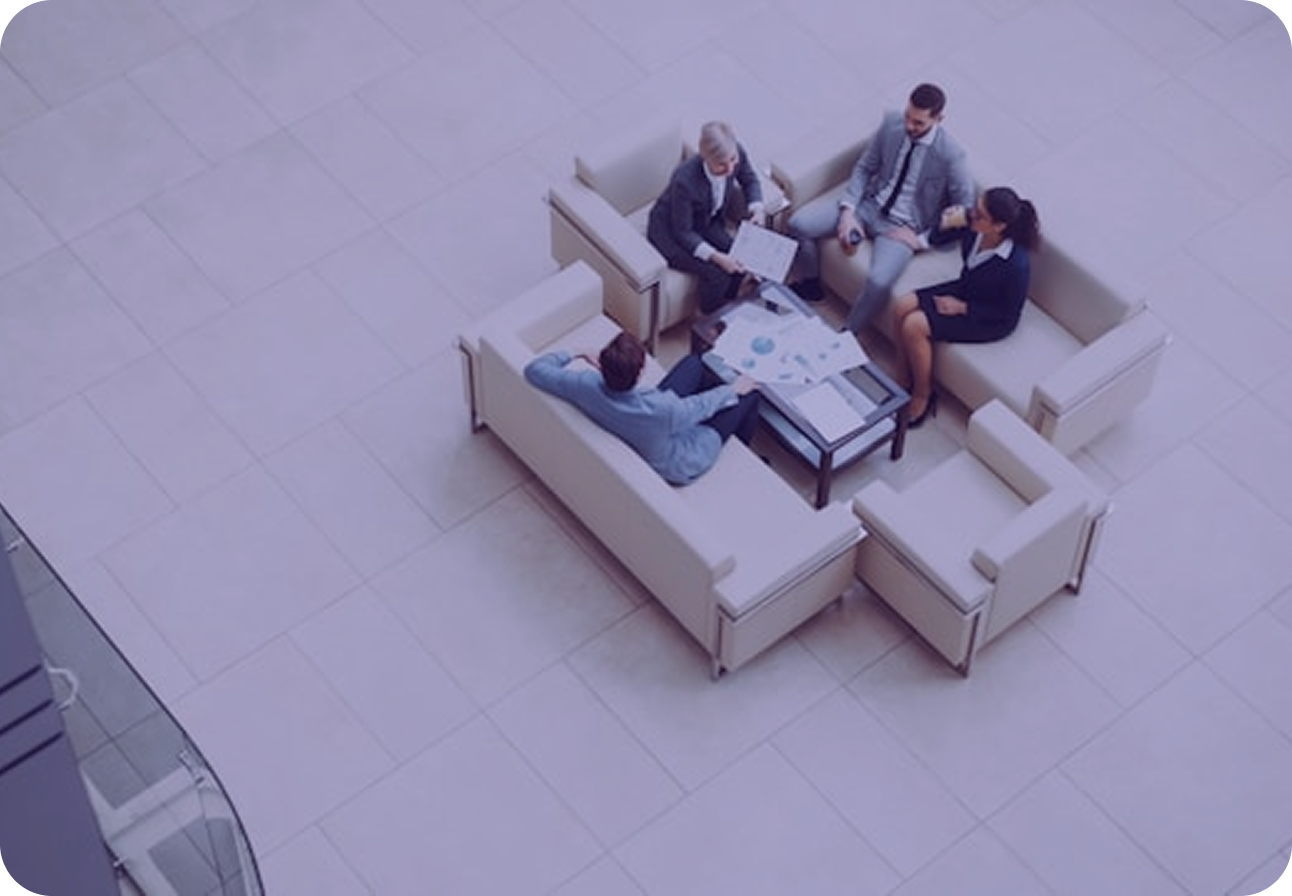 Overhead view of four colleagues meeting on couches in an office lobby, charts spread across the coffee table